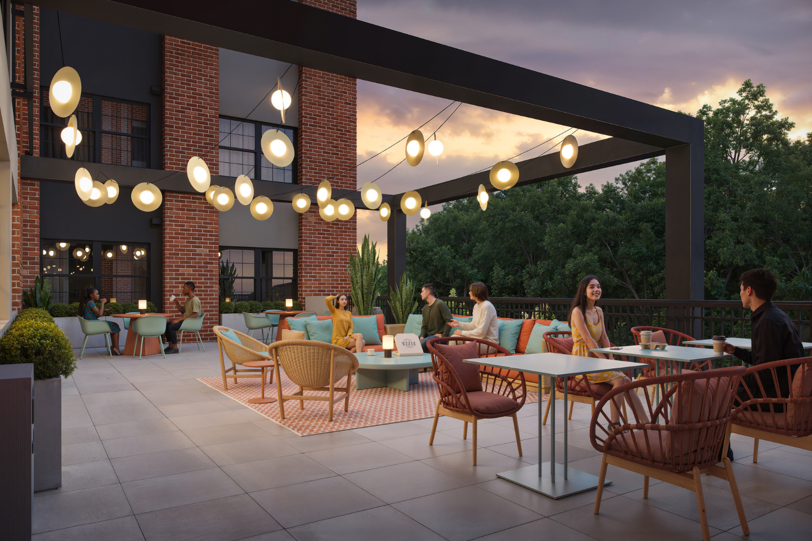 Outdoor resident lounge with comfortable seating, café tables, decorative lighting, and gathering spaces overlooking wooded views at dusk.